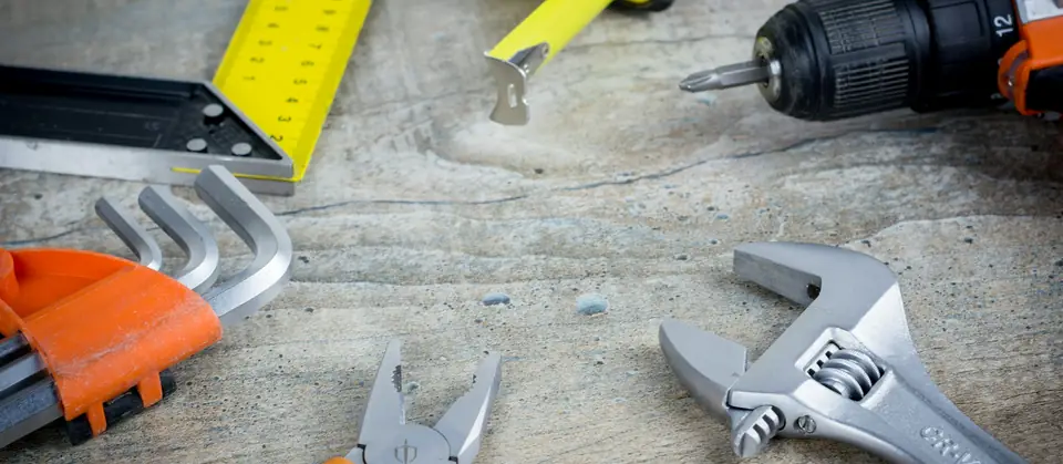 Hand tools, a cordless drill, tape measure and wrench laid out on a workbench