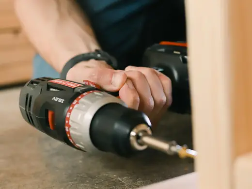 A cordless drill driving a screw into furniture