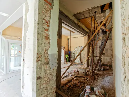 A tradesman on a ladder working inside a room being renovated